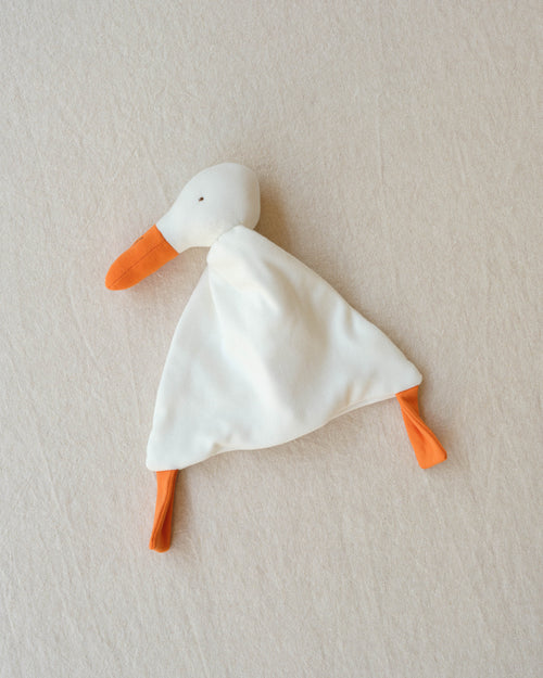 Small white duck toy with orange beak and feet on a beige background
