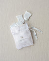 White baby booties and socks in a drawstring bag on a beige background