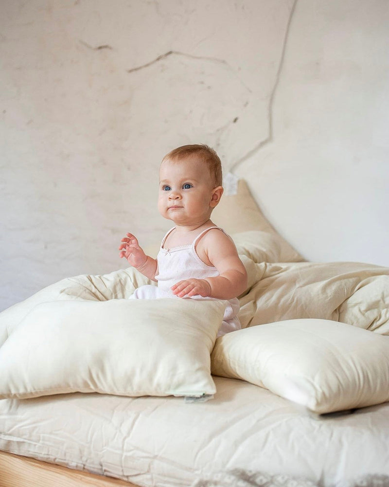 Baby sitting on a bed with white pillows and bedding