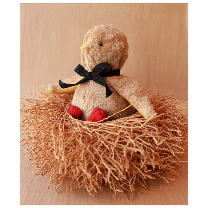 Stuffed bird toy with a black bow in a nest on a wooden surface