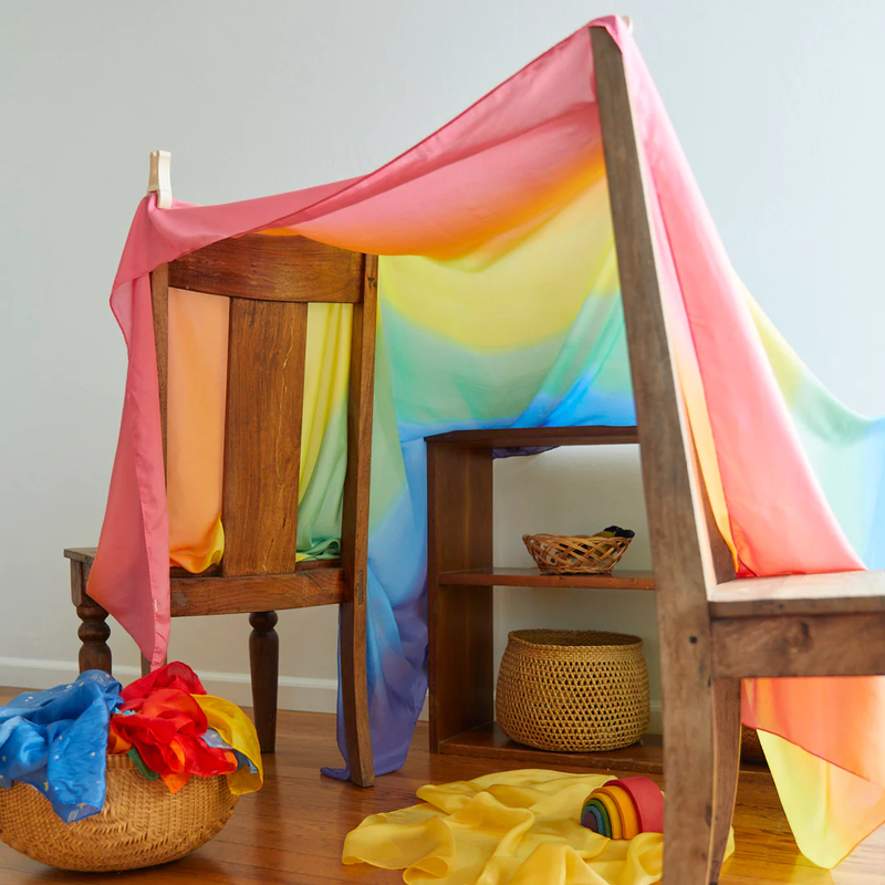 Colorful rainbow fabric draped over a wooden chair and shelf, with toys scattered on the floor.