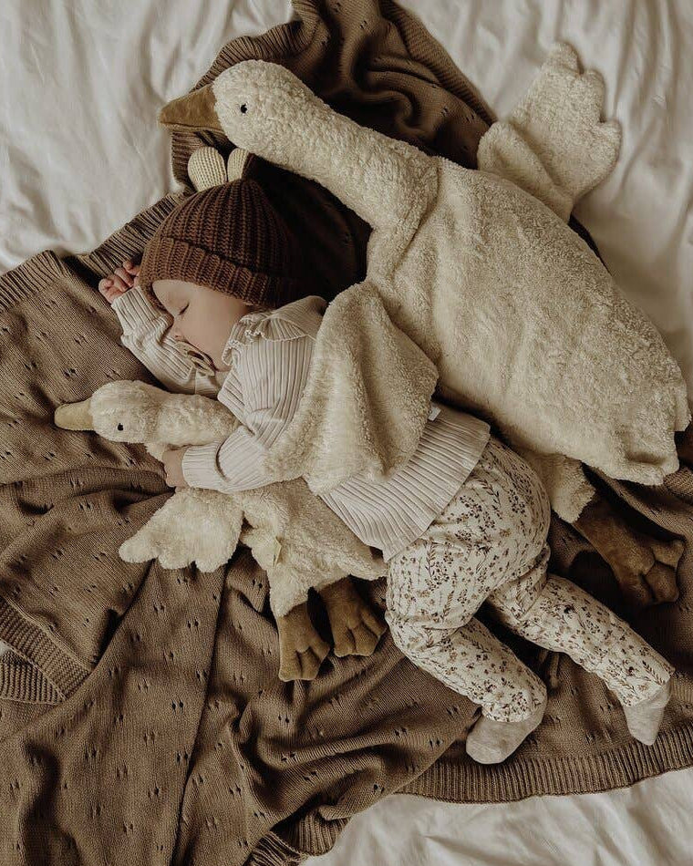 Child wrapped in a blanket with plush toys on a bed