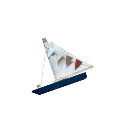 A small wooden toy sailboat with a white sail, colorful pennant bunting, and a blue hull, resting on a textured beige knit blanket.