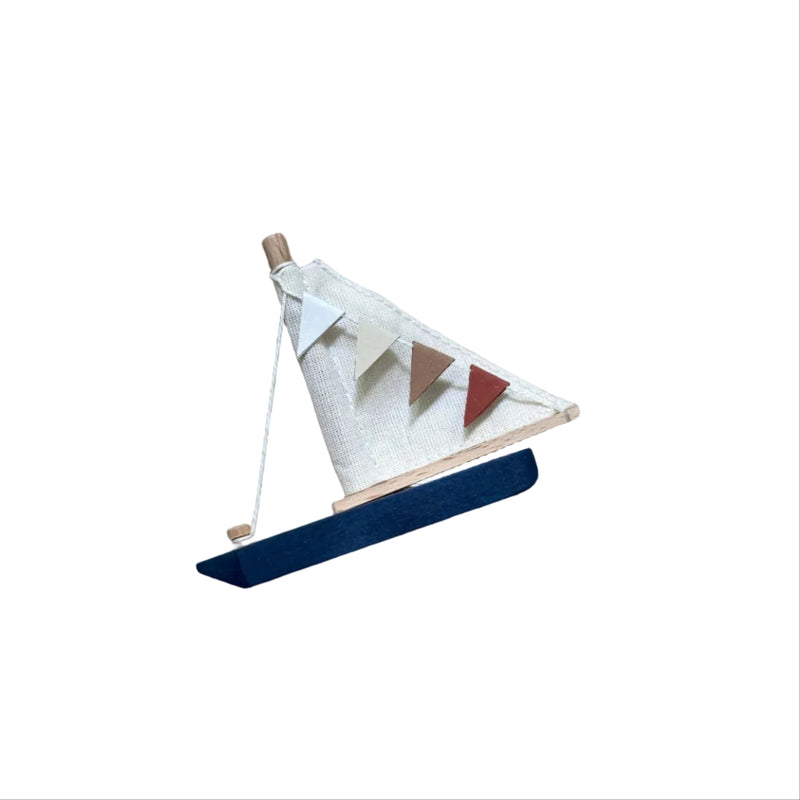 A small wooden toy sailboat with a white sail, colorful pennant bunting, and a blue hull, resting on a textured beige knit blanket.