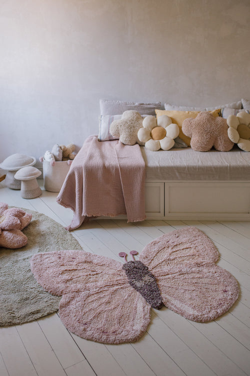 Children's room with a butterfly rug on the floor and a bed with decorative pillows in the background.