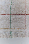 Close-up of a textured washable rug with plaid pattern and fringes on a white background
