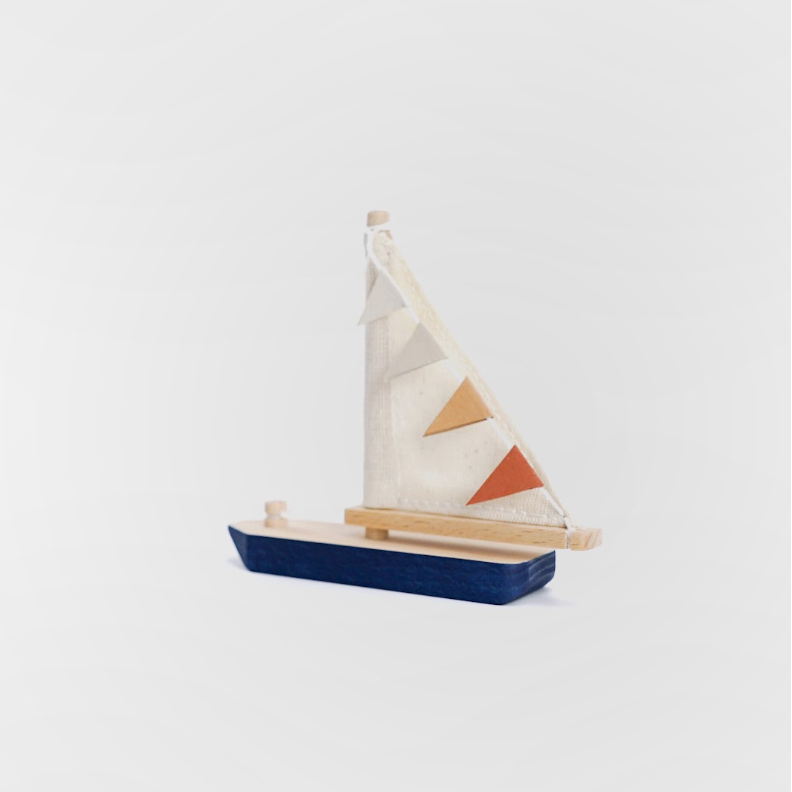 A small wooden toy sailboat with a dark blue hull, natural wood mast and deck, and a cream-colored sail decorated with geometric triangle patterns in beige and rust orange, set against a plain light gray background.