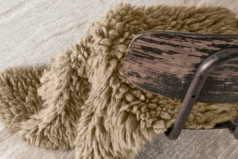 Close-up of a wooden chair with a textured beige cushion on a light wood floor.