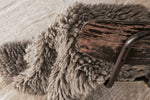 Close-up of a textured blanket draped over a wooden chair on a textured surface.