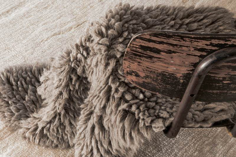 Close-up of a textured blanket draped over a wooden chair on a textured surface.