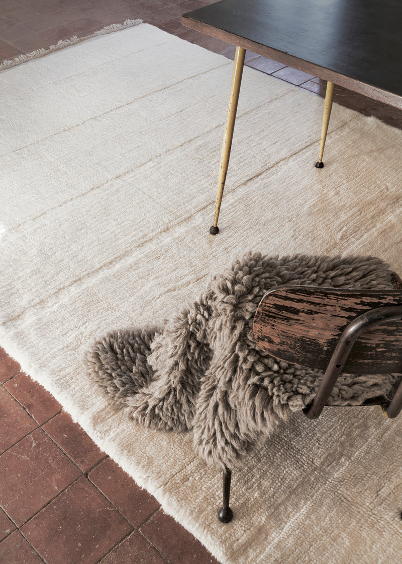 Beige rug with a wooden stool and fur throw on a tiled floor