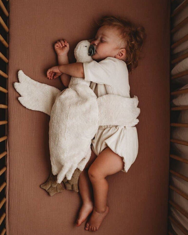Baby sleeping with a plush swan toy on a brown crib