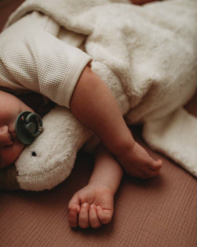 Child's arm and foot resting on a plush toy with a blanket in the background
