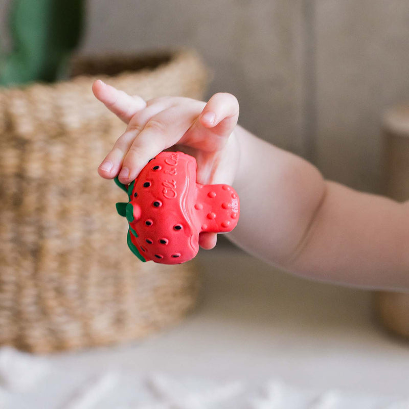Child's hand holding a red strawberry-shaped object with green leaves against a blurred background