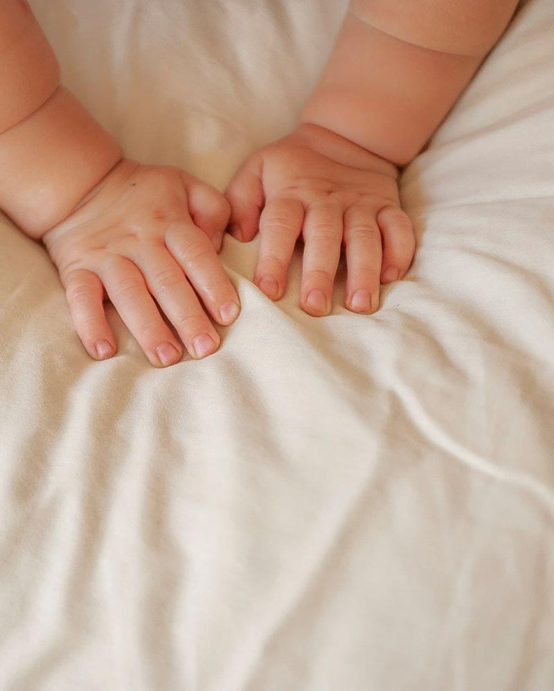 Two pairs of baby hands holding each other on a soft beige fabric background
